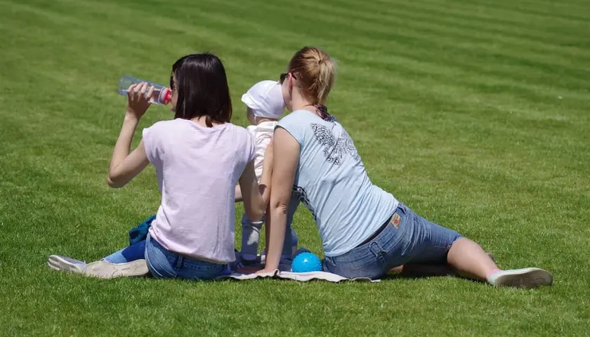 Dwie kobiety i dziecko siedzą na trawie. Jedna pije wodę, druga przytula dziecko. Czas na relaks i naukę, jak przestać się wszystkim przejmować.