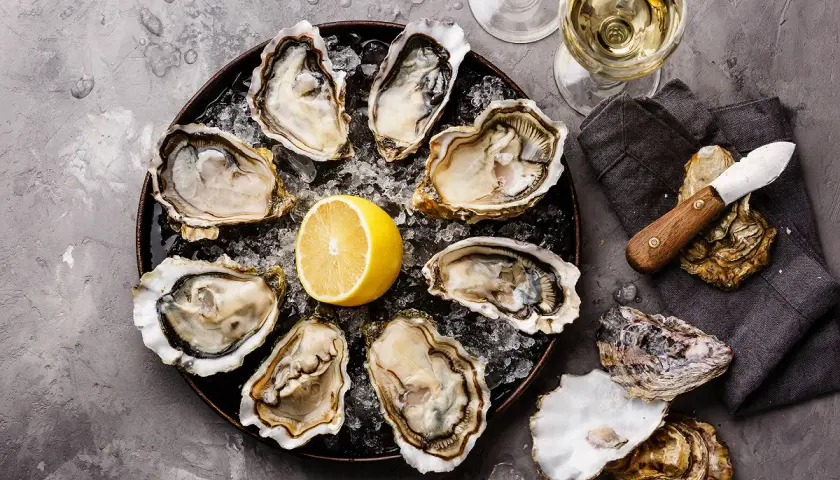 Plateau d'huîtres fraîches avec citron, deux verres de vin blanc, parfait pour le meilleur vin blanc pour fruits de mer.