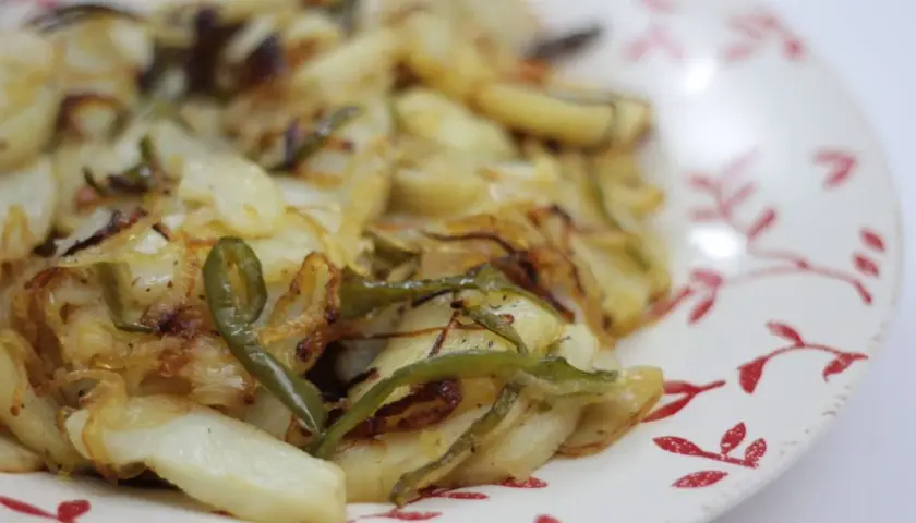 Plato de patatas panaderas al horno con cebolla y pimientos verdes, recién sacadas del horno y listas para disfrutar.