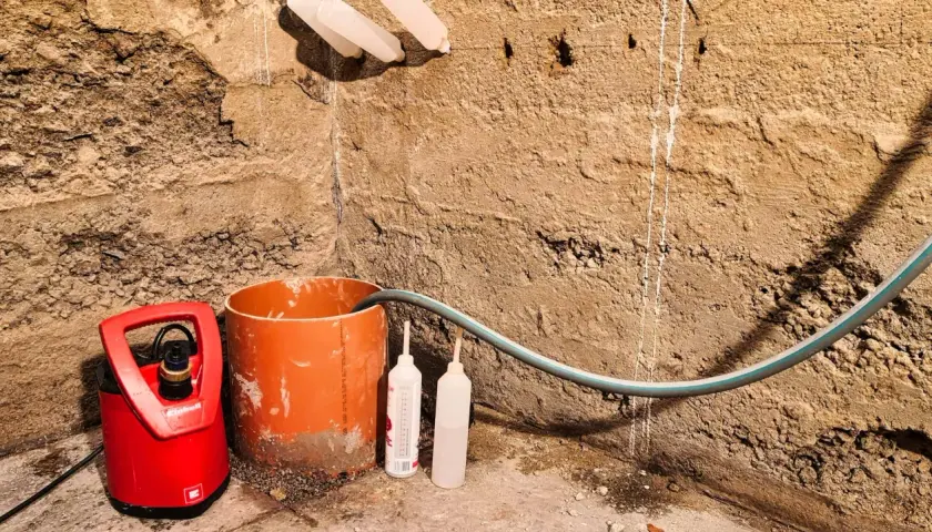 Rote Tauchpumpe mit Schlauch und Rohr zur Vorbereitung des Grundwasser abpumpen. Zwei leere Flaschen stehen daneben.