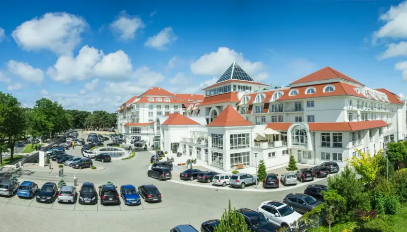 Elegancki hotel 5 gwiazdkowy nad morzem z przestronnym parkingiem pełnym samochodów.