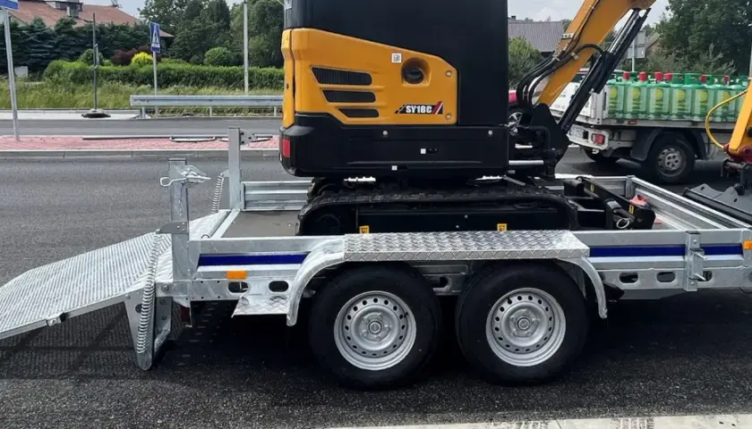 Żółta mini koparka SY18C na przyczepie z rampą. Waga maszyny pozwala na łatwy transport.