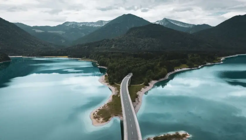 Brücke über türkisfarbenen See, umgeben von bewaldeten Bergen. Ein malerischer Ort für besondere Ausflugsziele.