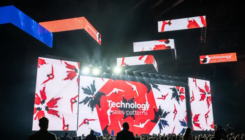 Wielkie ekrany na scenie pokazują ludzi w czerwonych strojach, tworzących wzory. To inspiracja, jak zarabiać na zdjęciach, wykorzystując kreatywność i technologię.