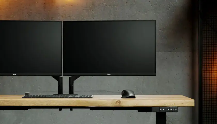 Dwa monitory LG na regulowanym biurku, zamontowane na uchwycie z mocowaniem **standard VESA**. Obok klawiatura i myszka.