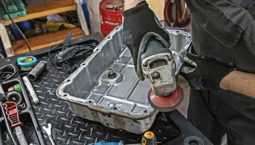 Mechanik szlifuje miskę olejową skrzyni biegów, przygotowując ją do wymiany oleju.