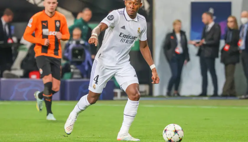 Piłkarz Realu Madryt w białej koszulce z numerem 4, David Alaba, prowadzi piłkę. W tle widać zawodnika Szachtara Donieck w pomarańczowej koszulce. To obraz jednego z najlepszych obrońców świata.