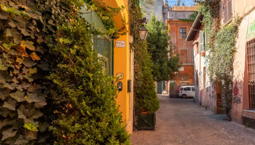 Un vicolo pittoresco tra le vie di Roma centro, con edera rampicante, edifici colorati e un'auto bianca parcheggiata.