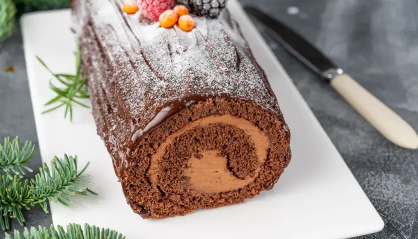 Bûche de Noël au chocolat, parfaite pour une recette génoise bûche moelleuse. Garnie de fruits rouges et de sucre glace.