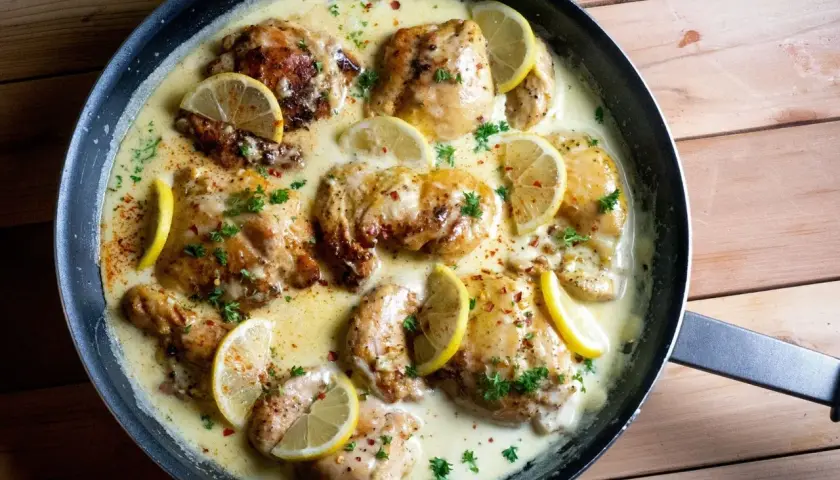 Succulento petto di pollo al limone in padella, guarnito con fette di limone fresco e prezzemolo tritato.