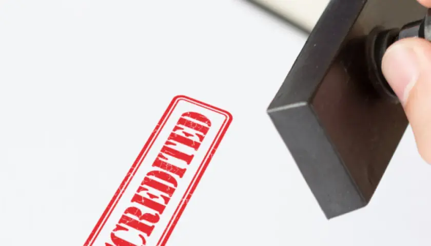 A hand presses a stamp, leaving a red "ACCREDITED" mark. This signifies official MPA accreditation.