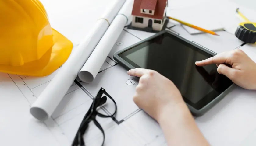 Nowoczesne technologie budowy domu: tablet, plany, model domu, kask i okulary.