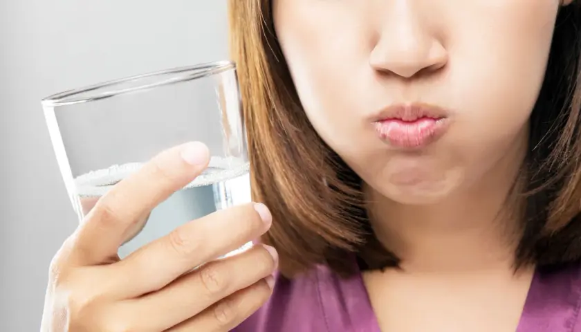 Frau mit geschlossenen Augen hält ein Glas Wasser und spült sich den Mund aus. Ein erfrischendes salzwasser am morgen Ritual.