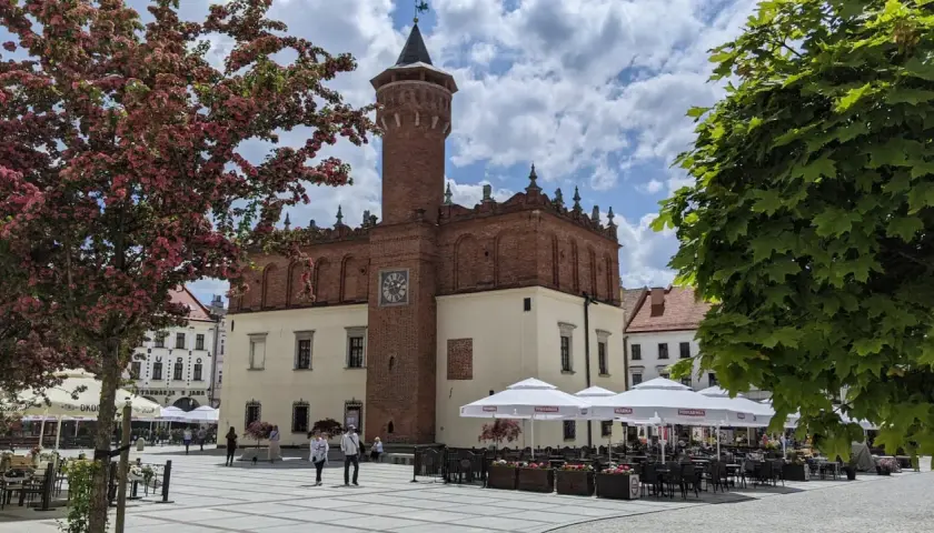 Rynek w Tarnowie z ratuszem i wieżą widokową. Wiosną kwitną drzewa, a kawiarnie zapraszają do ogródków.