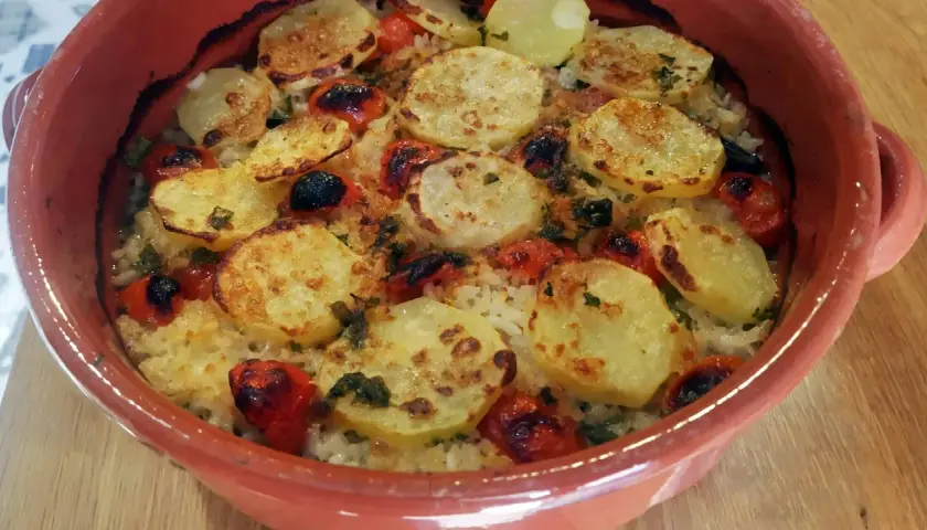 Piatto di riso patate e cozze cotto al forno, con pomodorini e erbe aromatiche, servito in una terrina di terracotta.