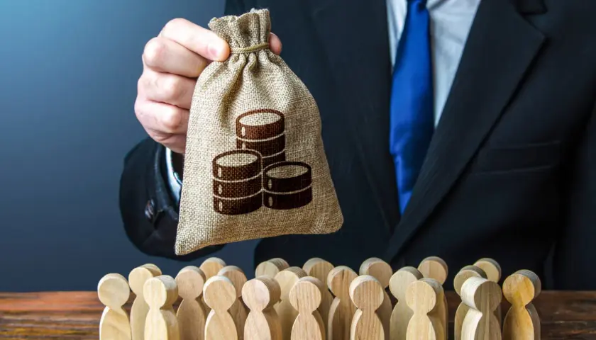 Hr manager w garniturze trzyma worek z pieniędzmi nad grupą drewnianych ludzików.