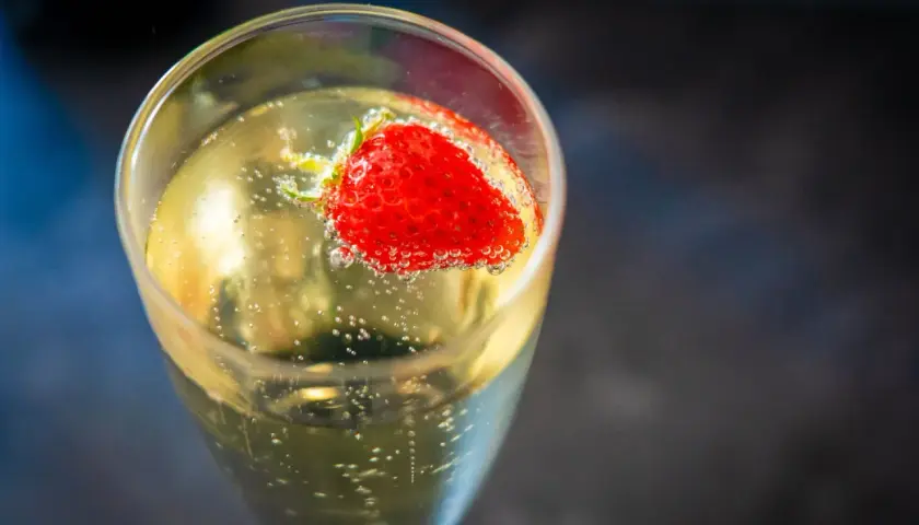 Une fraise flotte dans un verre de soupe angevine pétillante, créant une image rafraîchissante.