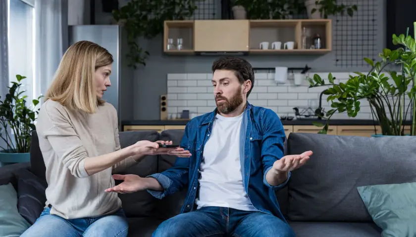 Kobieta z pretensjami pokazuje mężczyźnie telefon, sugerując, że była żona nie spłaca kredytu hipotecznego.