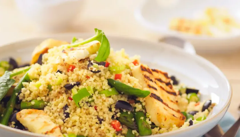 Un piatto colorato di cous cous con verdure miste, olive nere e cubetti di formaggio grigliato.