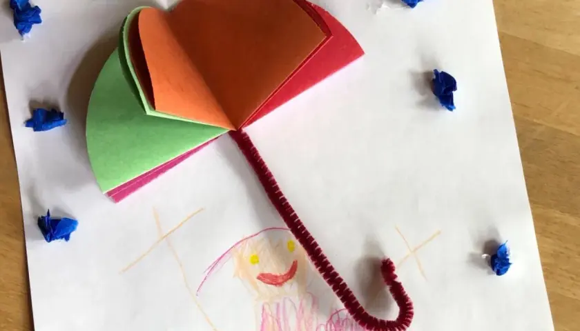 Buntes Papier und Pfeifenreiniger ergeben einen tollen Regenschirm zum Basteln. Kleine blaue Tupfer symbolisieren Regentropfen.