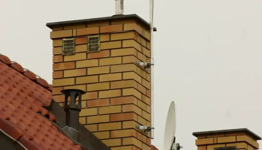 Ceglanego komina z dwoma kratkami wentylacyjnymi, które mogą służyć jako odpowietrzenie kanalizacji. Na dachu widać antenę satelitarną.