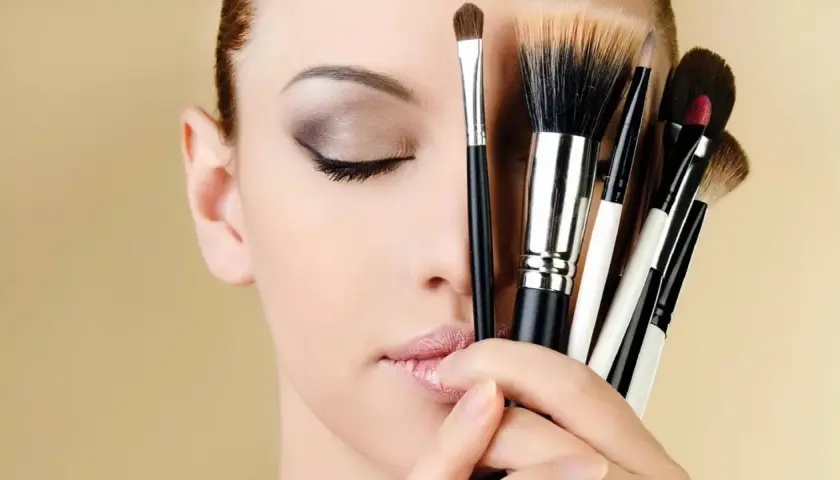 Mujer con ojos cerrados y varios pinceles de maquillaje, inspirando ideas de maquillaje.
