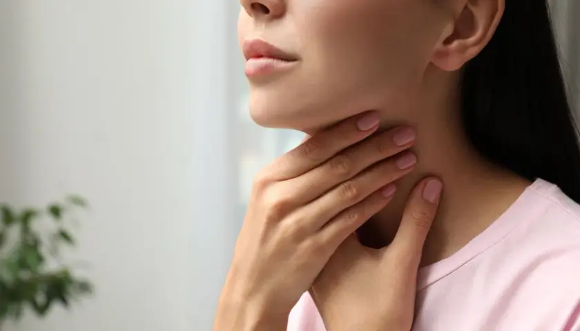 Kobieta dotyka szyi, być może odczuwając dyskomfort związany z tarczycą, który może być leczony np. thyrozolem.