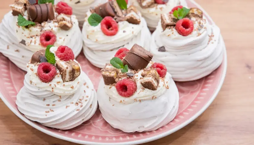 Słodkie mini pavlova z bitą śmietaną, malinami i kawałkami czekolady na różowym talerzu.
