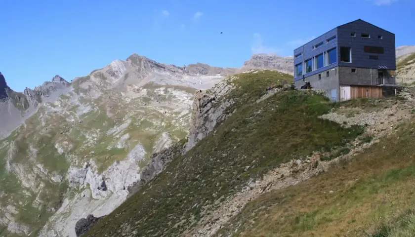 Moderne Hütte am Hang, Teil der Tour des Muverans, mit steilen Felswänden und grünen Bergwiesen im Hintergrund.