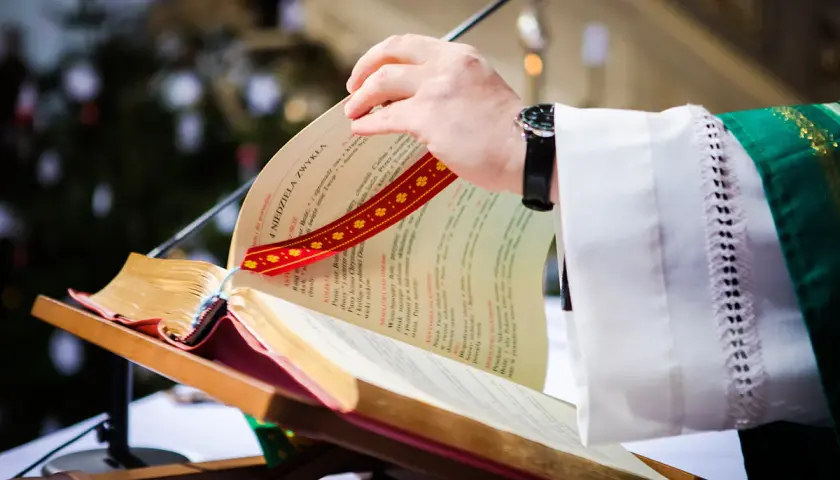 Dłoń księdza przewracająca kartki księgi liturgicznej na pulpicie.