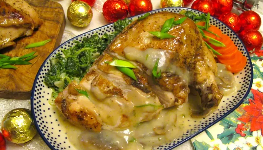 Pieczona pierś z kurczaka w sosie, podana ze szpinakiem i marchewką, ozdobiona szczypiorkiem.