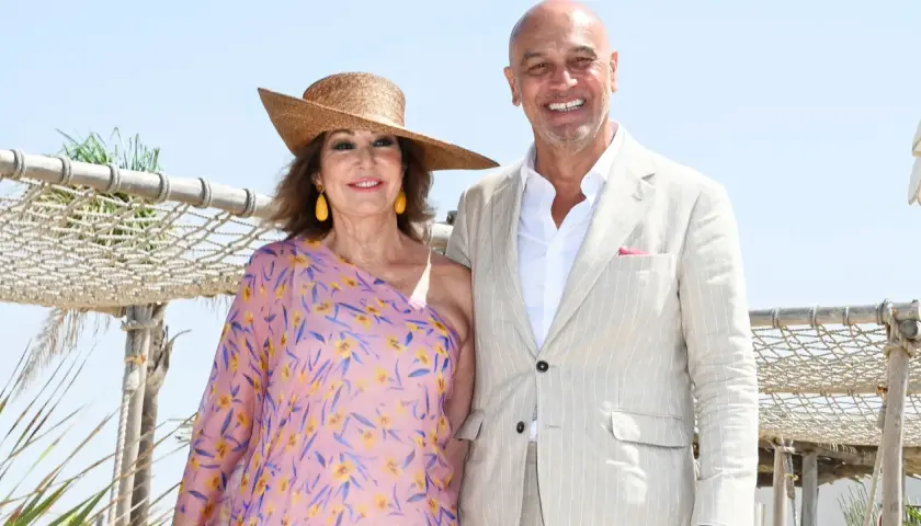 Ana Rosa Quintana y su marido celebran la boda de su hijo. Ella luce un vestido floral y sombrero, él un traje claro.