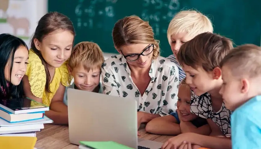 Nauczycielka z uczniami przy laptopie. Szukają informacji, gdzie znaleźć sprawdziany z nowej ery.