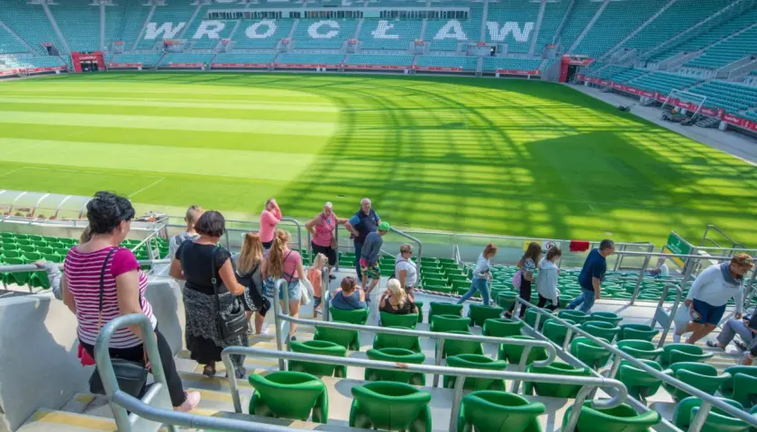 Grupa ludzi wchodzi na zielone trybuny stadionu. W tle widać murawę i napis "WROCŁAW".