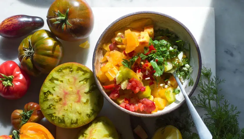 En skål med färgglad pico de gallo, omgiven av olika sorters tomater.