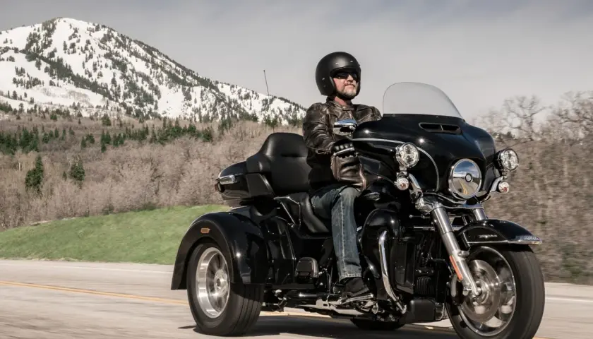 Mężczyzna w kasku i skórzanej kurtce jedzie czarnym motocyklem trójkołowym. W tle góry pokryte śniegiem. Kategoria L5e.