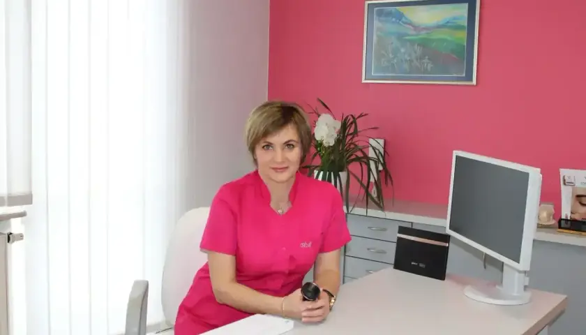 Lekarka w różowym uniformie siedzi przy biurku w gabinecie estetycznym.