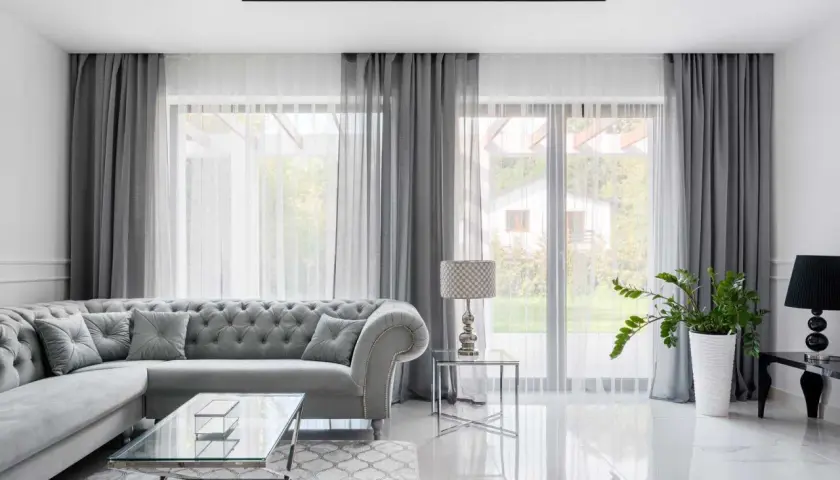 Eleganckie aranżacje okna w salonie: szara sofa, szklane stoliki i zasłony tworzą przytulną atmosferę.