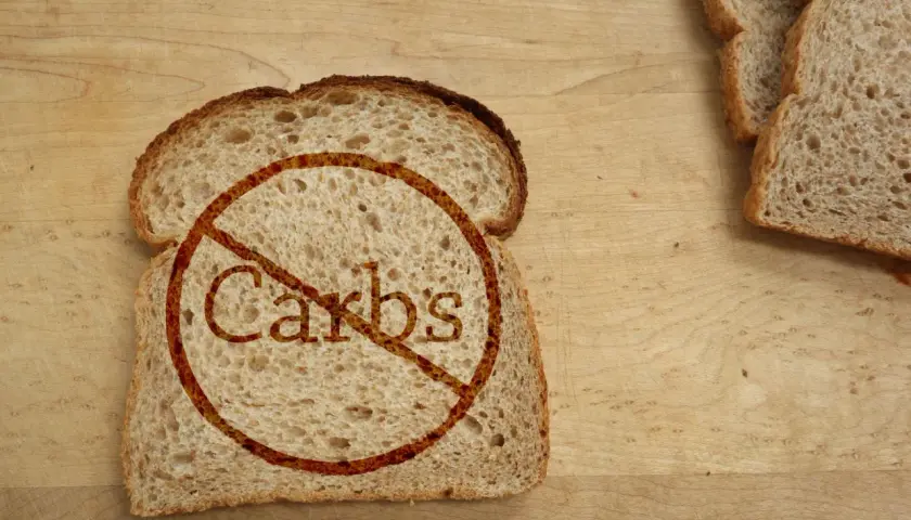Kromka chleba z przekreślonym napisem "Carbs". Idealne dla osób szukających produktów bez węglowodanów, tabela z nimi może być pomocna.