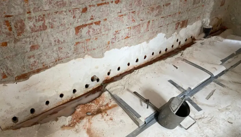 Bohrungen in der Kellerwand deuten auf Maßnahmen gegen aufsteigende Feuchtigkeit hin. Wasser sammelt sich am Boden.