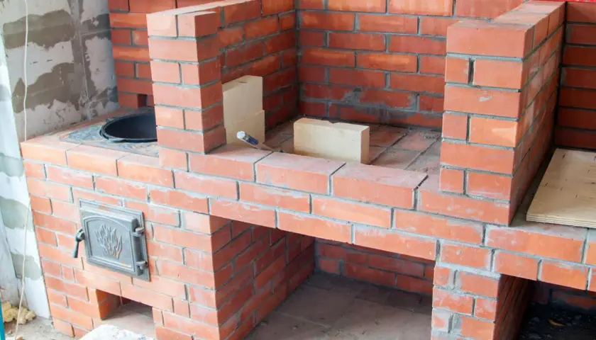 Construction d'un barbecue fait maison en briques rouges. Des briques supplémentaires et un niveau à bulle sont visibles sur le chantier.