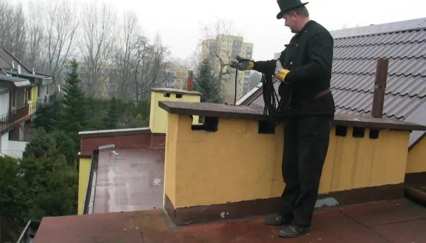 Kominiarz w cylindrze na dachu z liną. Czy kominiarz może dać mandat za zaniedbany komin?