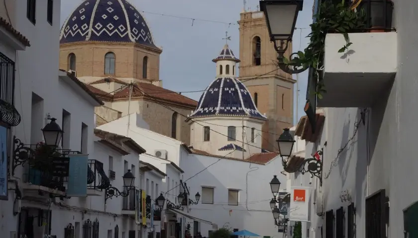 Calle estrecha con casas blancas y cúpulas azules, un ejemplo de los pueblos más bonitos de Alicante.