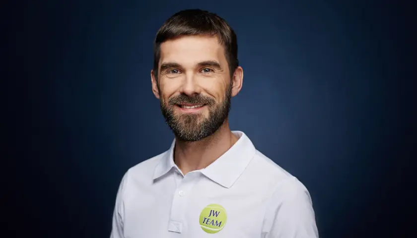 Paweł Habrat, uśmiechnięty mężczyzna z brodą, w białej koszulce polo z logo "JW TEAM".