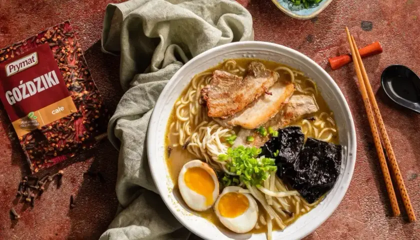 Jak zrobić ramen? Aromatyczny bulion, makaron, jajko na pół, plastry boczku i nori. Obok paczka goździków Prymat.