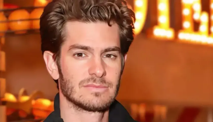 Andrew Garfield, avec une barbe naissante, pose devant des lumières chaudes. On spécule sur son prochain film.