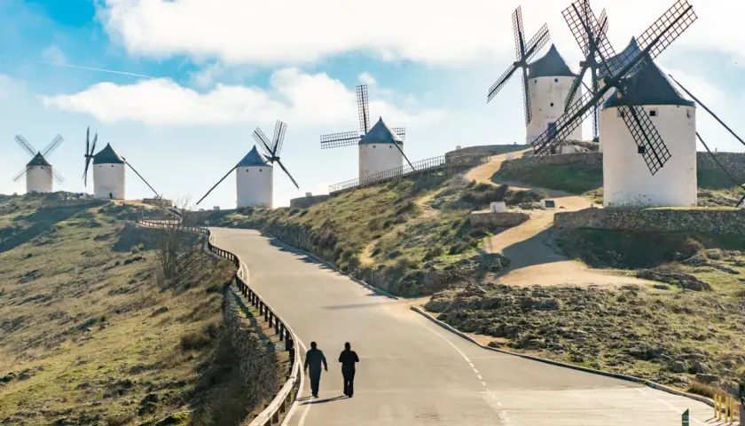 Molinos de viento en la ruta de Don Quijote, con dos personas caminando por un camino.