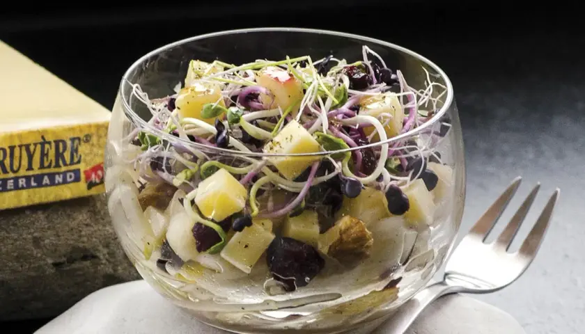Deliciosa ensalada de endivias con trozos de queso Gruyère, arándanos y brotes frescos, servida en copa de cristal.