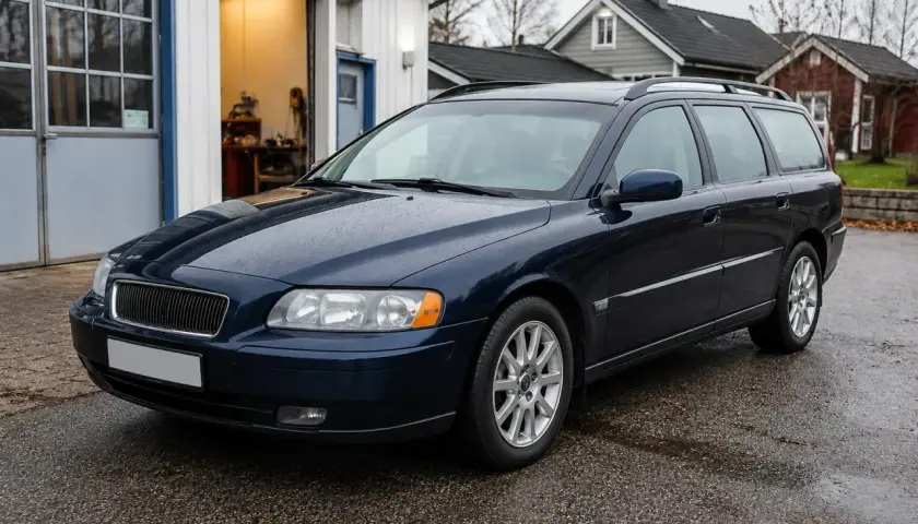 Mörkblå Volvo V70 2.0 Flexifuel står parkerad utanför en verkstad. Kanske är det ett problem med bilen som behöver åtgärdas.