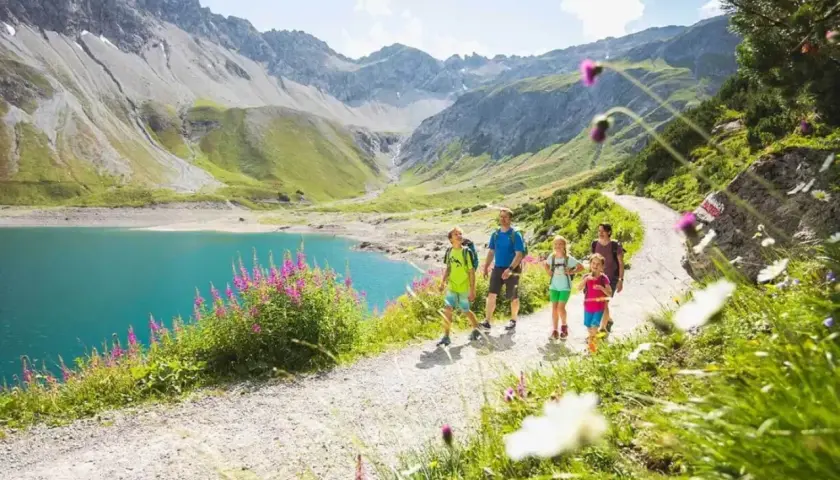 Familie genießt eine Wanderung im Brandnertal. Türkiser Bergsee, grüne Hänge und blühende Wiesen.